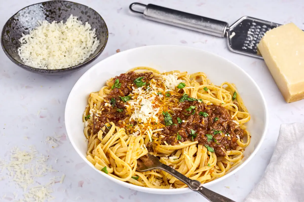 hvid skål med original spaghetti bolognese og linguine pasta med grana padano parmesan på toppen og ved siden af