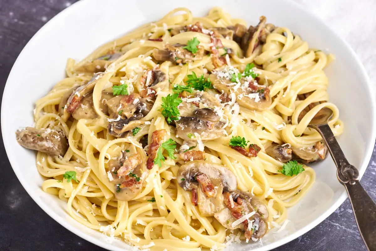 hvid tallerken med pasta med fløde, bacon og ristede champignoner