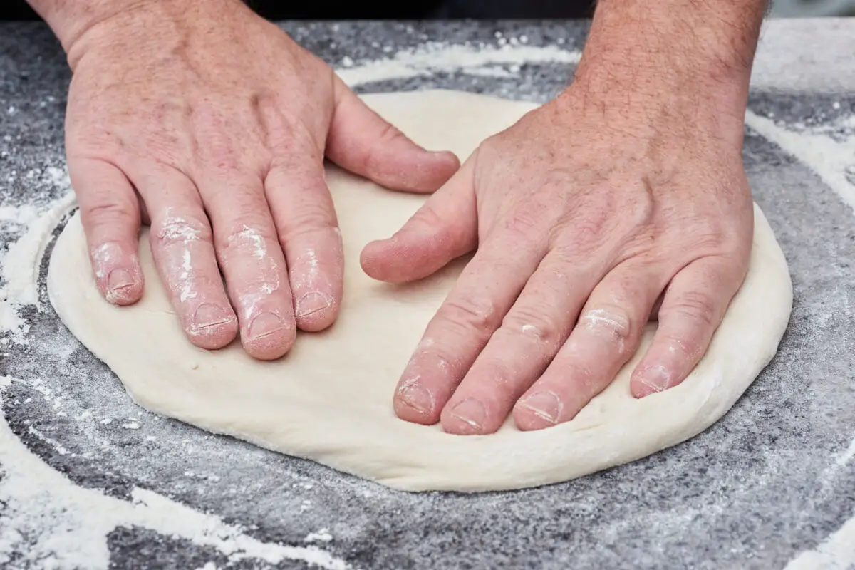hjemmelavet pizzadej til pizzabunde der trykkes ud med hænderne