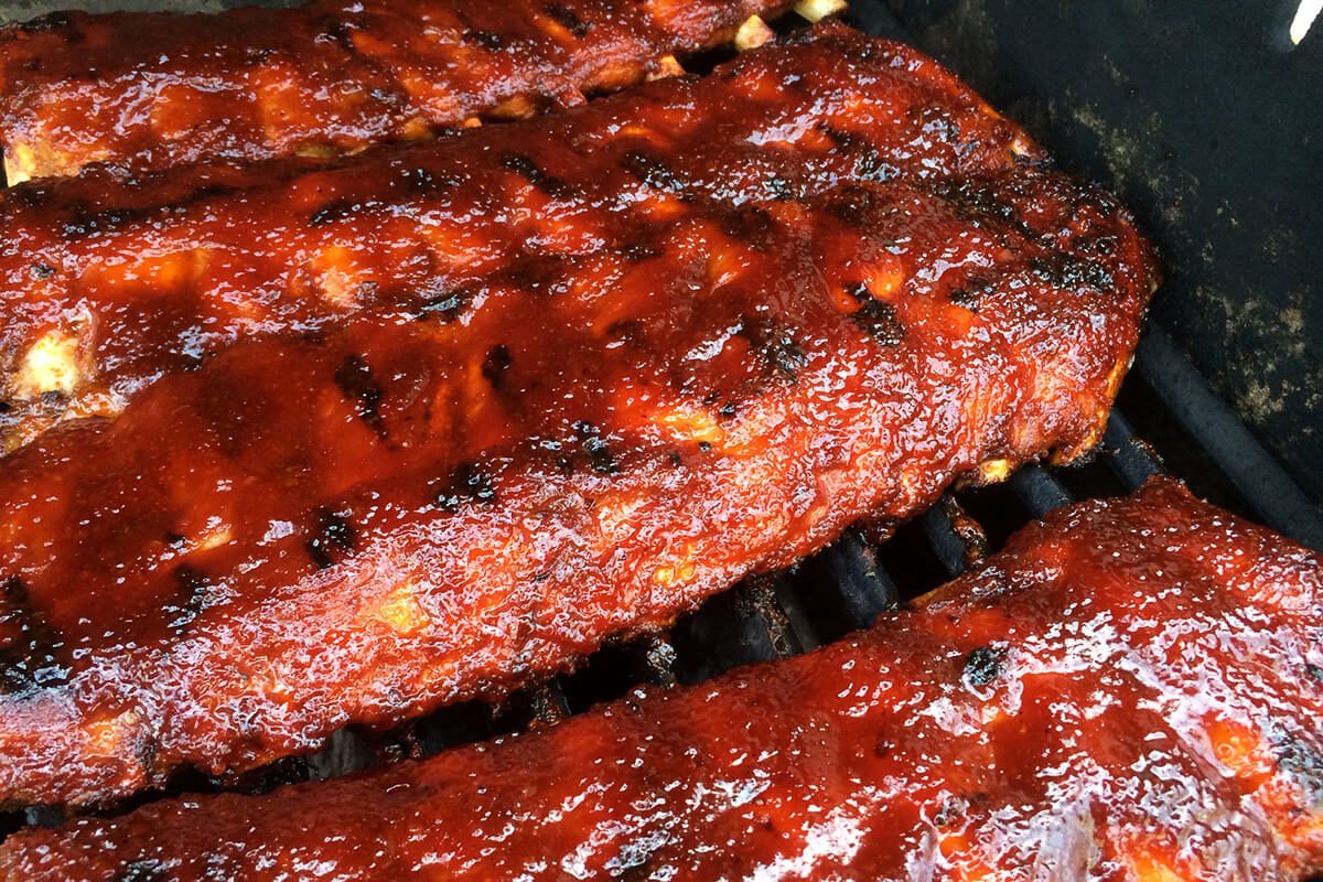 Snaskede spareribs på grill med barbecue sovs.
