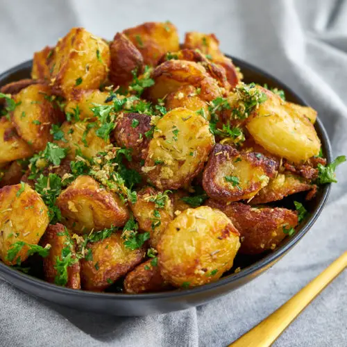 sprøde kartofler i ovn serveret i en lille skål med en ske.