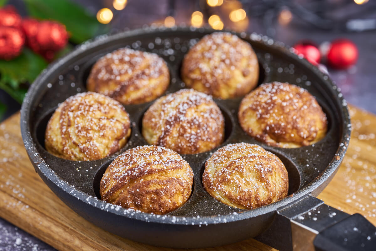 Hjemmelavet æbleskiver i æbleskivepande med flormelis og julepynt i baggrunden