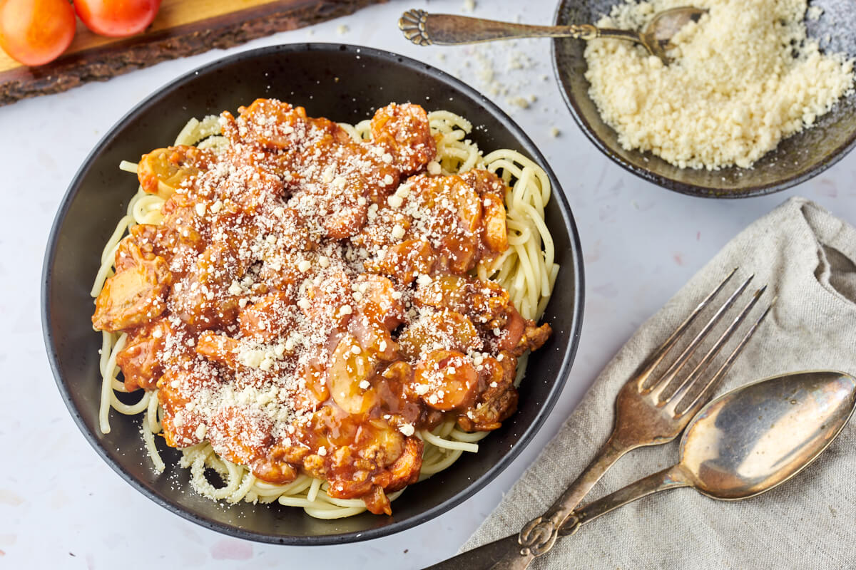 spaghetti med kødsovs i en sort skål med parmesan ovenpå