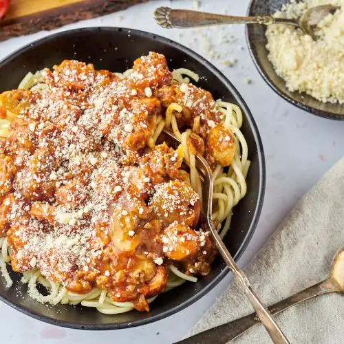 kims spaghetti med kødsovs med pølser og champignon i sort skål med parmesan ved siden af