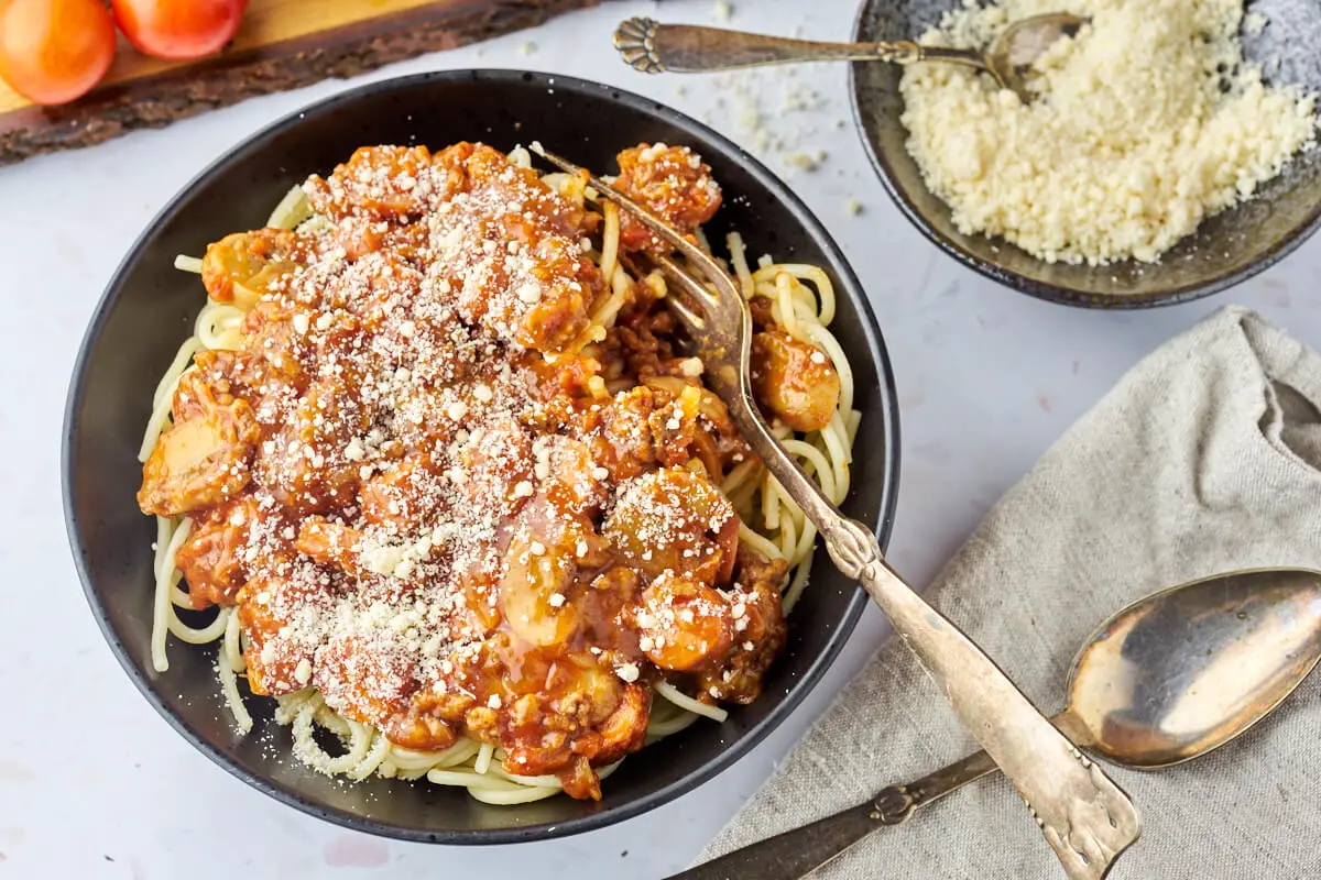 skål med spaghetti med kødsovs drysset med parmesan og gaffel i skålen