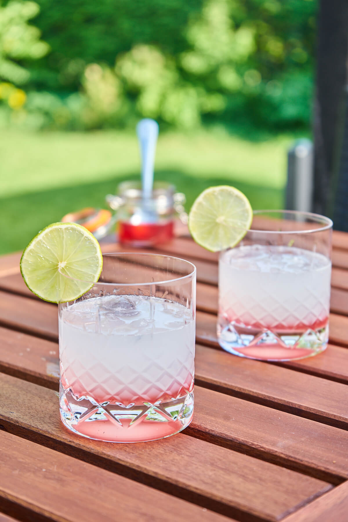 to rabarber gin hass cocktails på havebord med rabarbersirup og grøn have i baggrunden