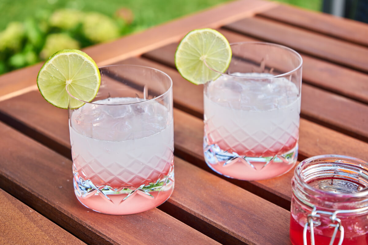to rabarber gin hass cocktails på havebord med rabarbersirup og limeskive på glasset