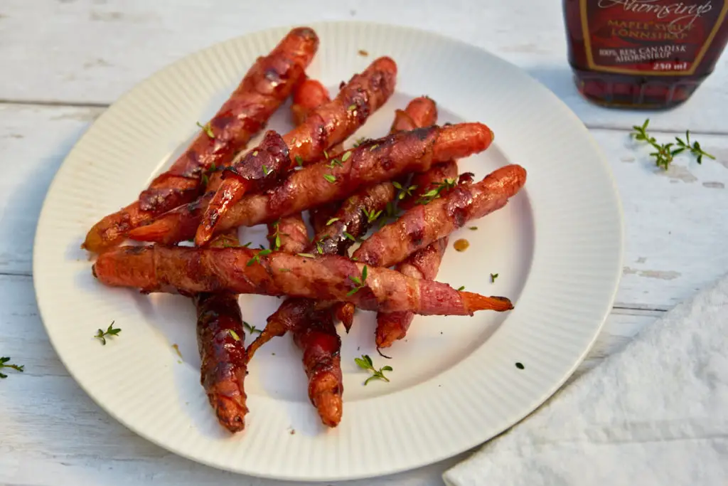 Grillede gulerødder med bacon, ahornsirup og timian på en hvid tallerken