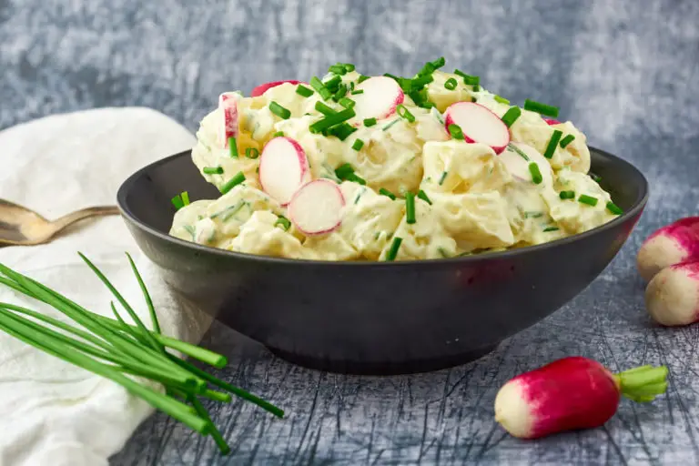 Kold kartoffelsalat med radiser og purløg i en sort skål