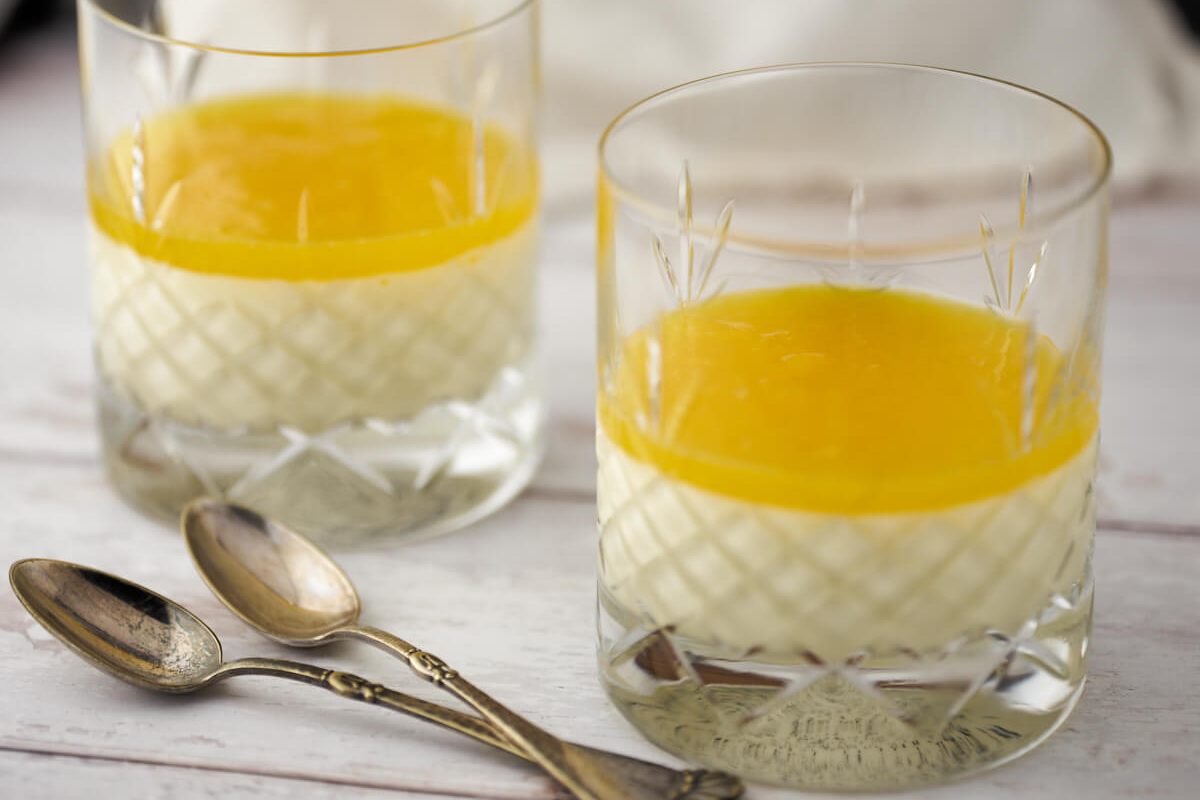 Panna cotta i glas med mango-gele pรฅ toppen og to skeer.
