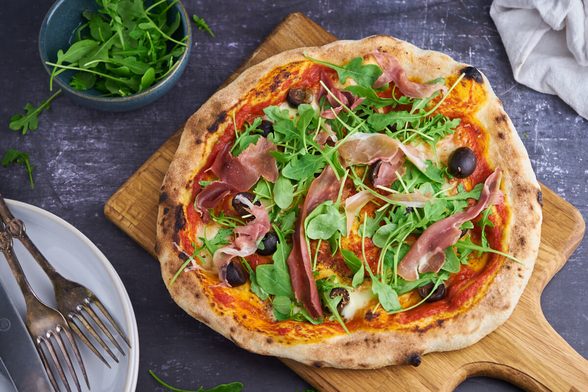 Hjemmelavet Pizza parma med tomatsovs parmaskinke og rucola salat samt oliven