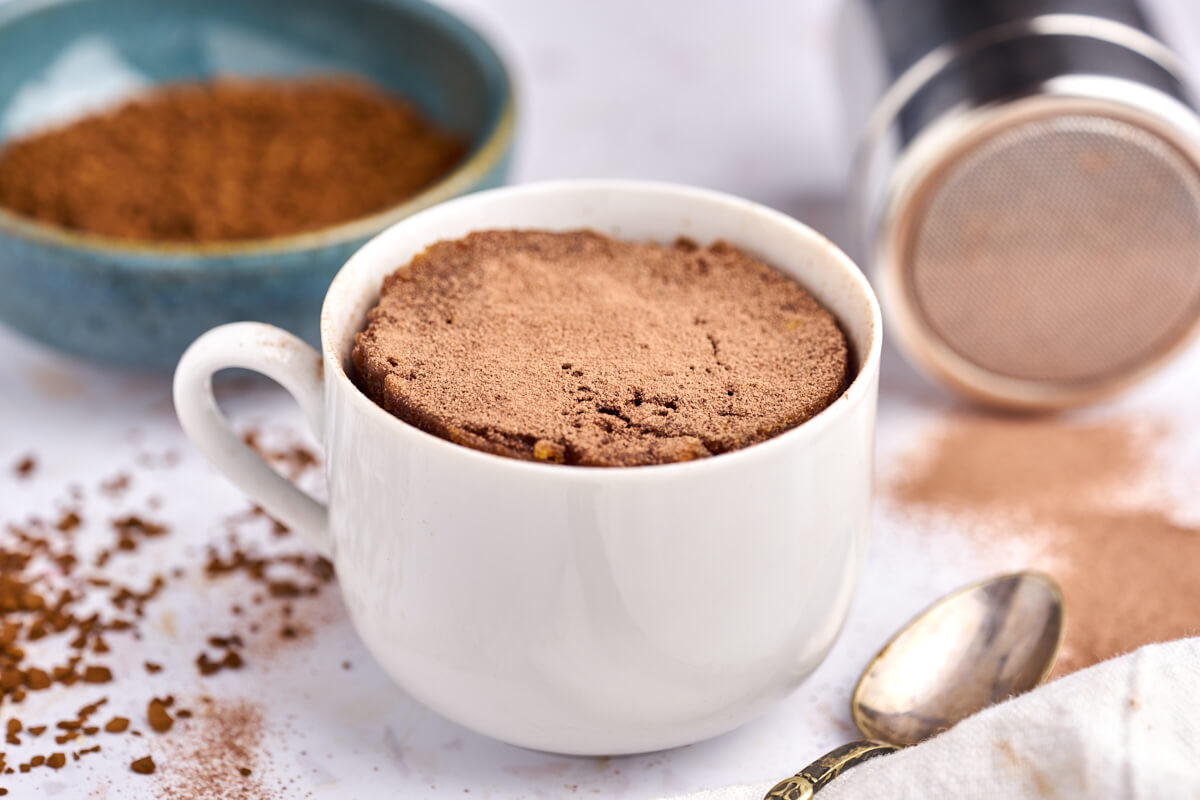 Cafe latte kage i kop bagt i mikroovn med instant kaffe og kakaopulver bagved