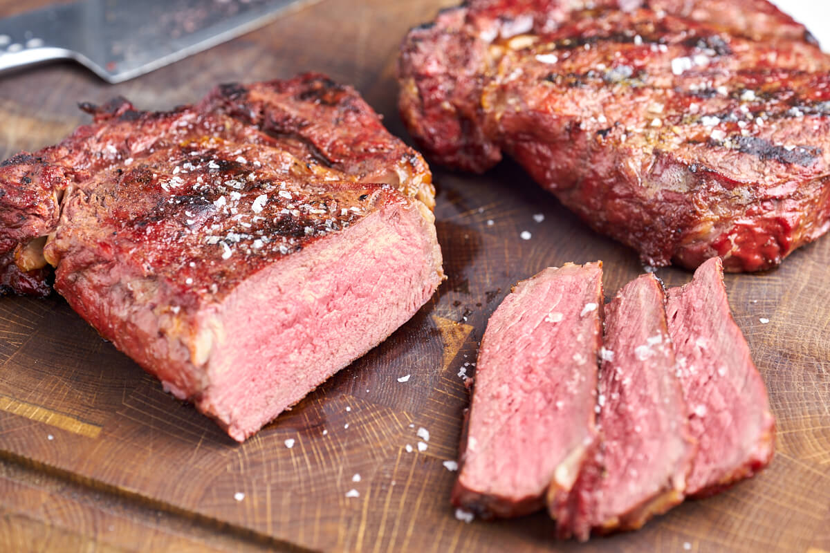 perfekt rosa ribeye på grill skåret i skiver med hel grilllet ribeye bøf i baggrunden