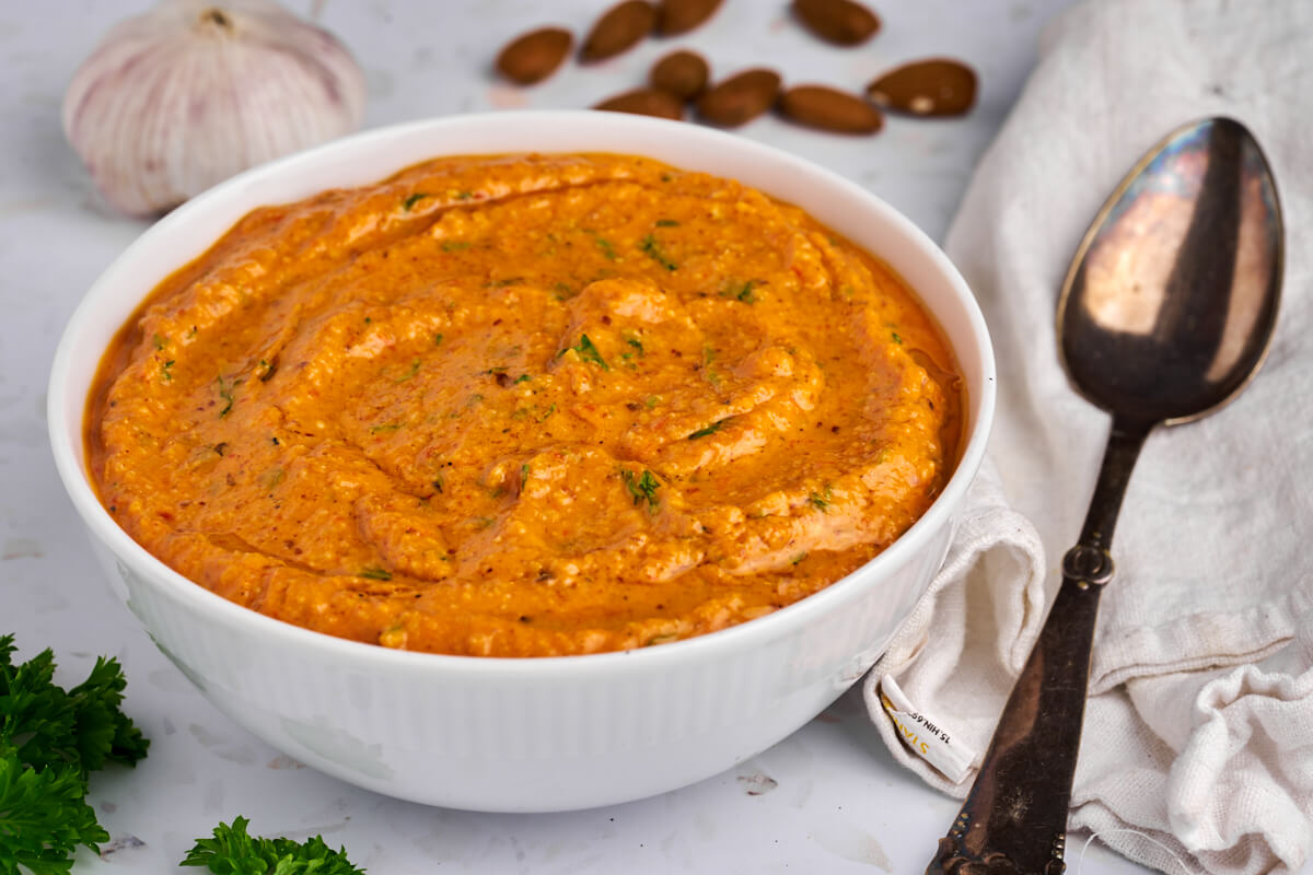romesco sauce med peberfrugt i hvid skål med mandler hvidløg og persille ved siden af.