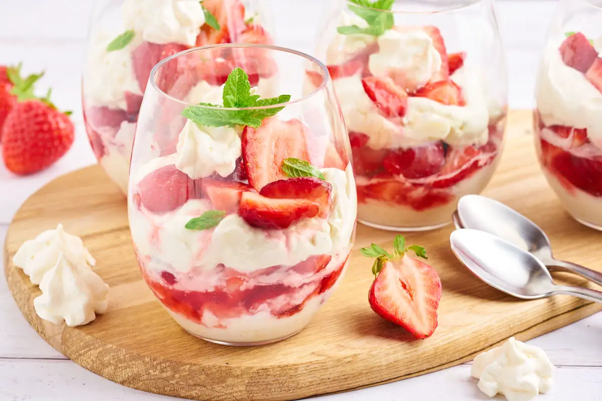 glas med eton mess dessert med lag af marinerede jordbær, flødecreme og marengs