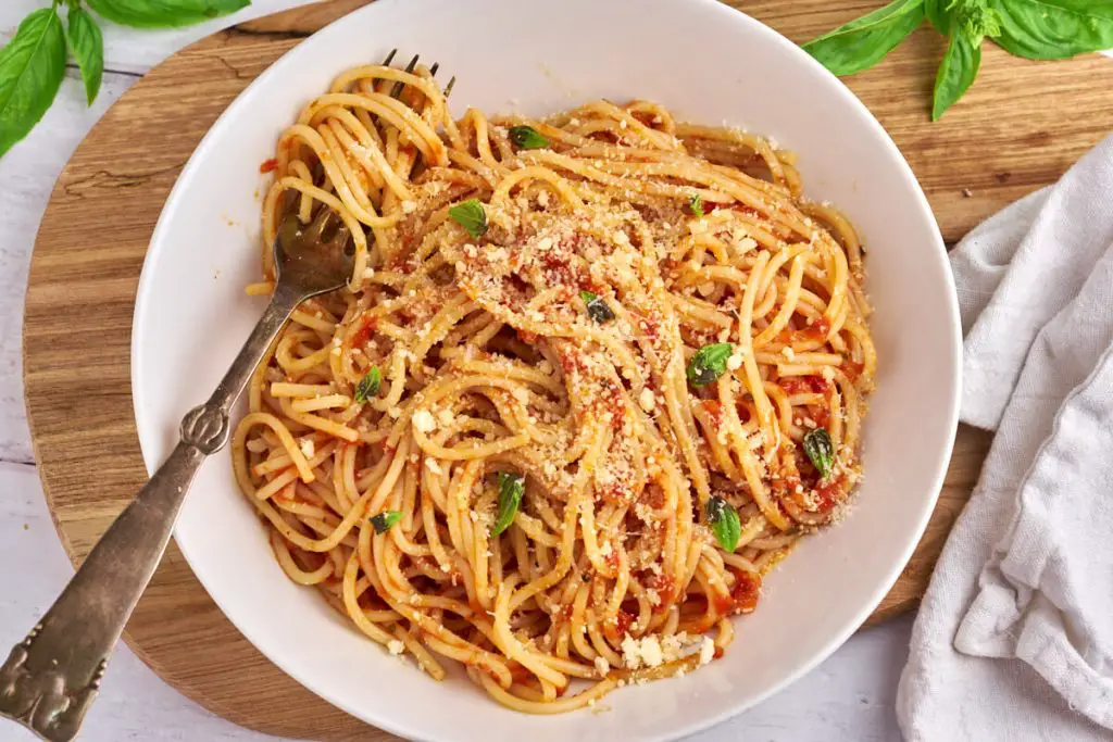 pasta pomodoro eller spaghetti med tomatsovs i tallerken med basilikum og parmesan på toppen