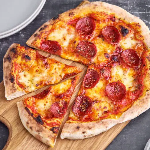 pepperoni pizza med tomatsovs og ost på skærebræt