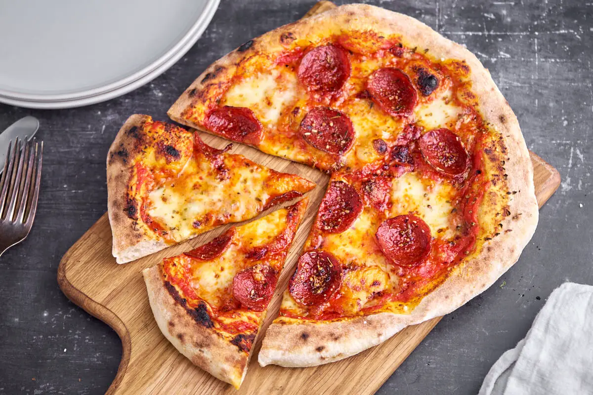 pepperoni pizza med tomatsovs og ost på skærebræt