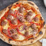 pizza med kødboller, rød peberfrugt, rødløg, tomatsovs og ost på skærebræt