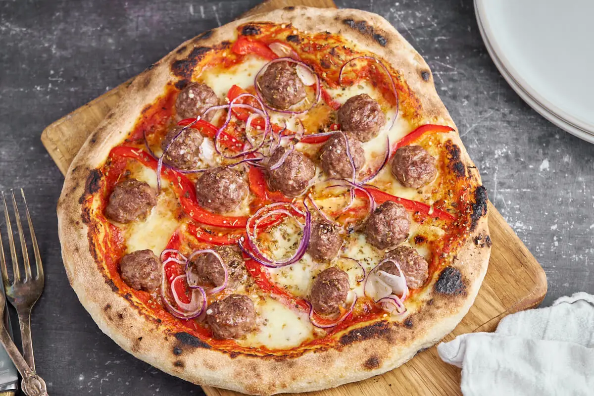 pizza med kødboller, rød peberfrugt, rødløg, tomatsovs og ost på skærebræt