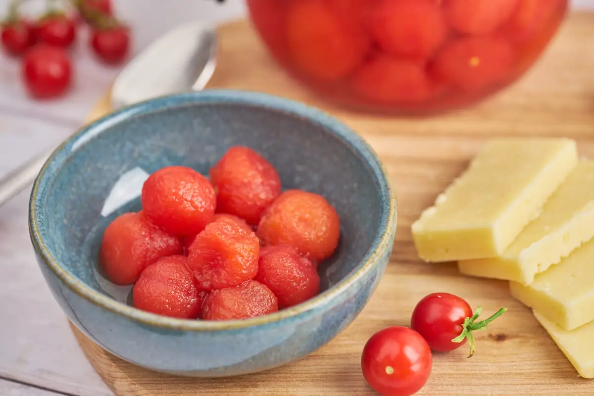 skål med syltede små tomater til ost med glas med cherrytomater og syltelage bagved