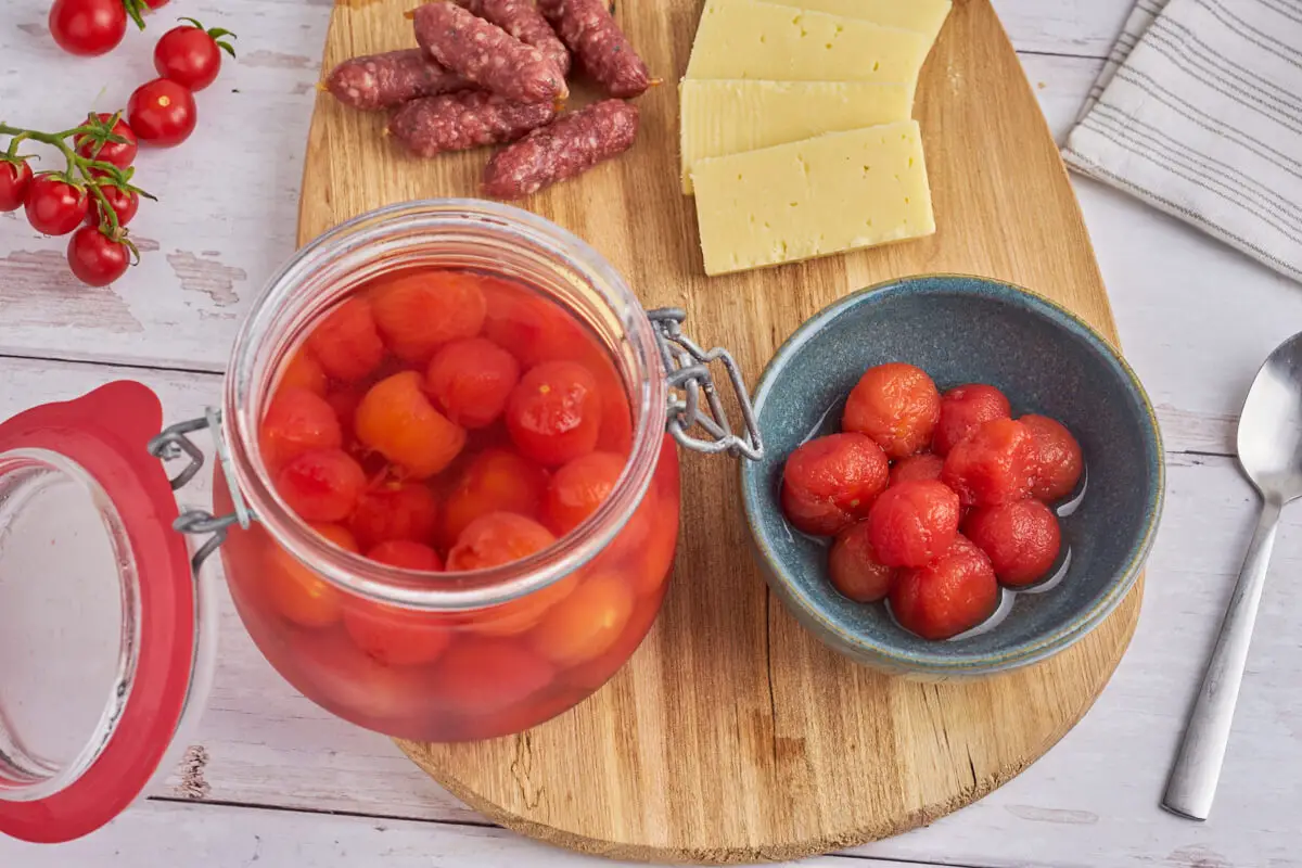 glas og skål med små syltede cherrytomater serveret til tapas og ost