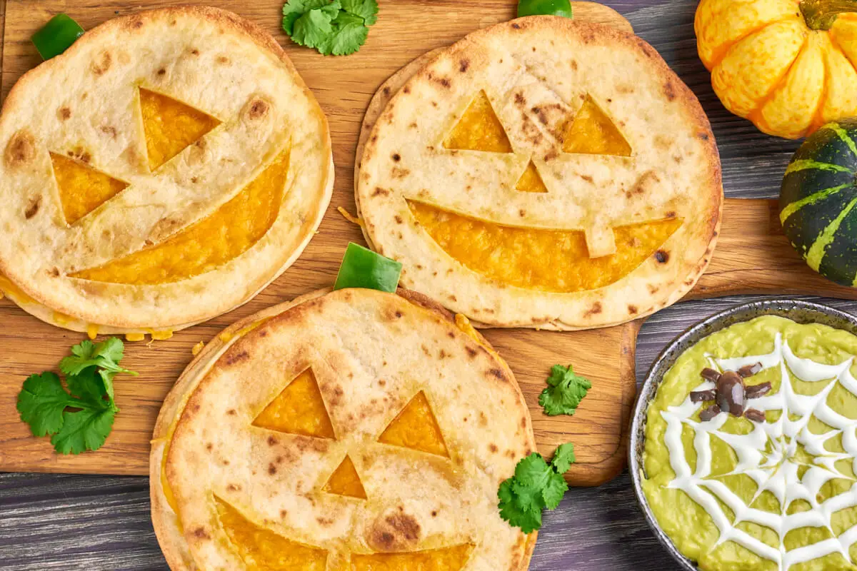 Jack o Lantern quesadillas like pumpkin lanterns with cheddar cheese inside and guacamole in bowl
