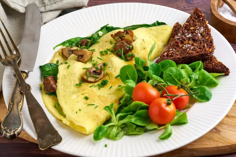 omelet med spinat og champignon serveret på tallerken med ristet rugbrød og salat