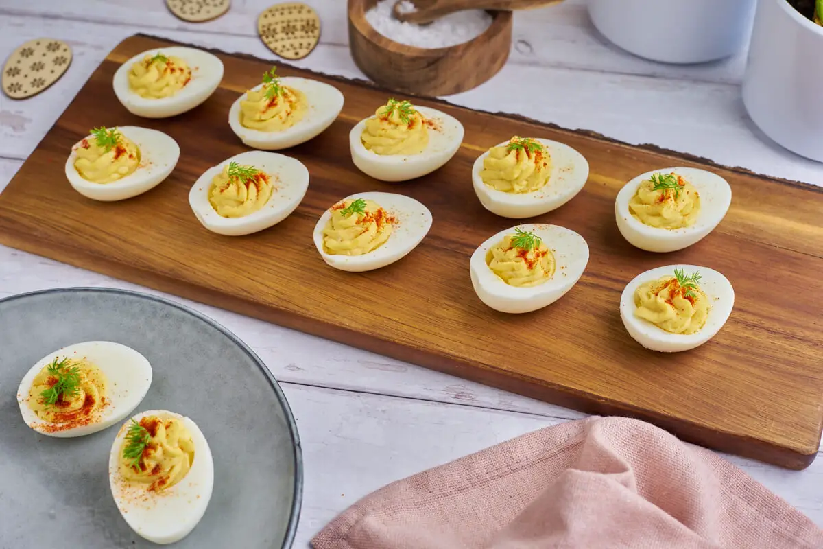 Djævleæg eller deviled eggs med fyld på træbræt med tallerken ved siden af