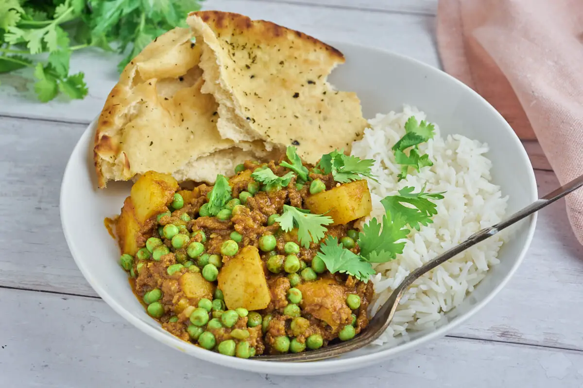 indisk keema aloo curry med hakket oksekød, kartofler og ærter serveret i tallerken med ris og naanbrød