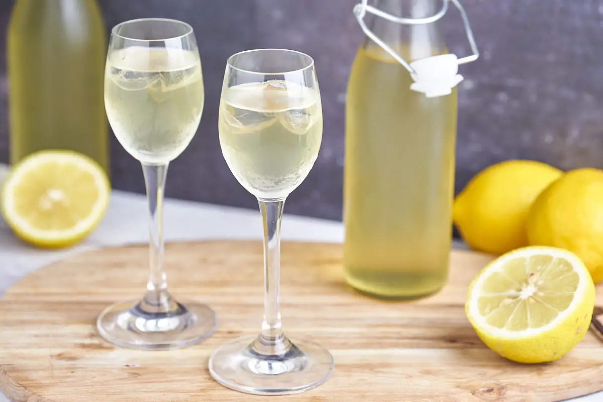glas med hjemmelavet citronlikør i på træbræt med flasker og citroner