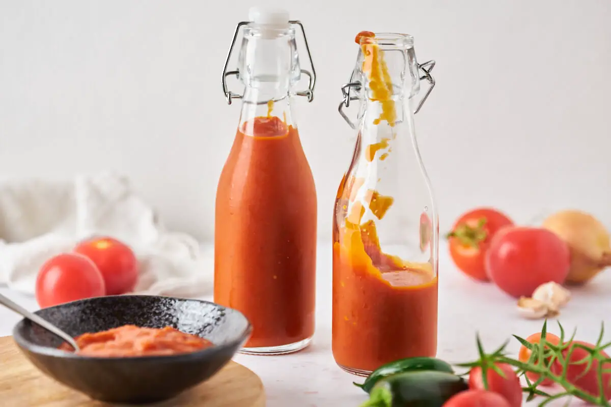 hjemmelavet tomatketchup i små flaske med skål med ketchup og friske tomater