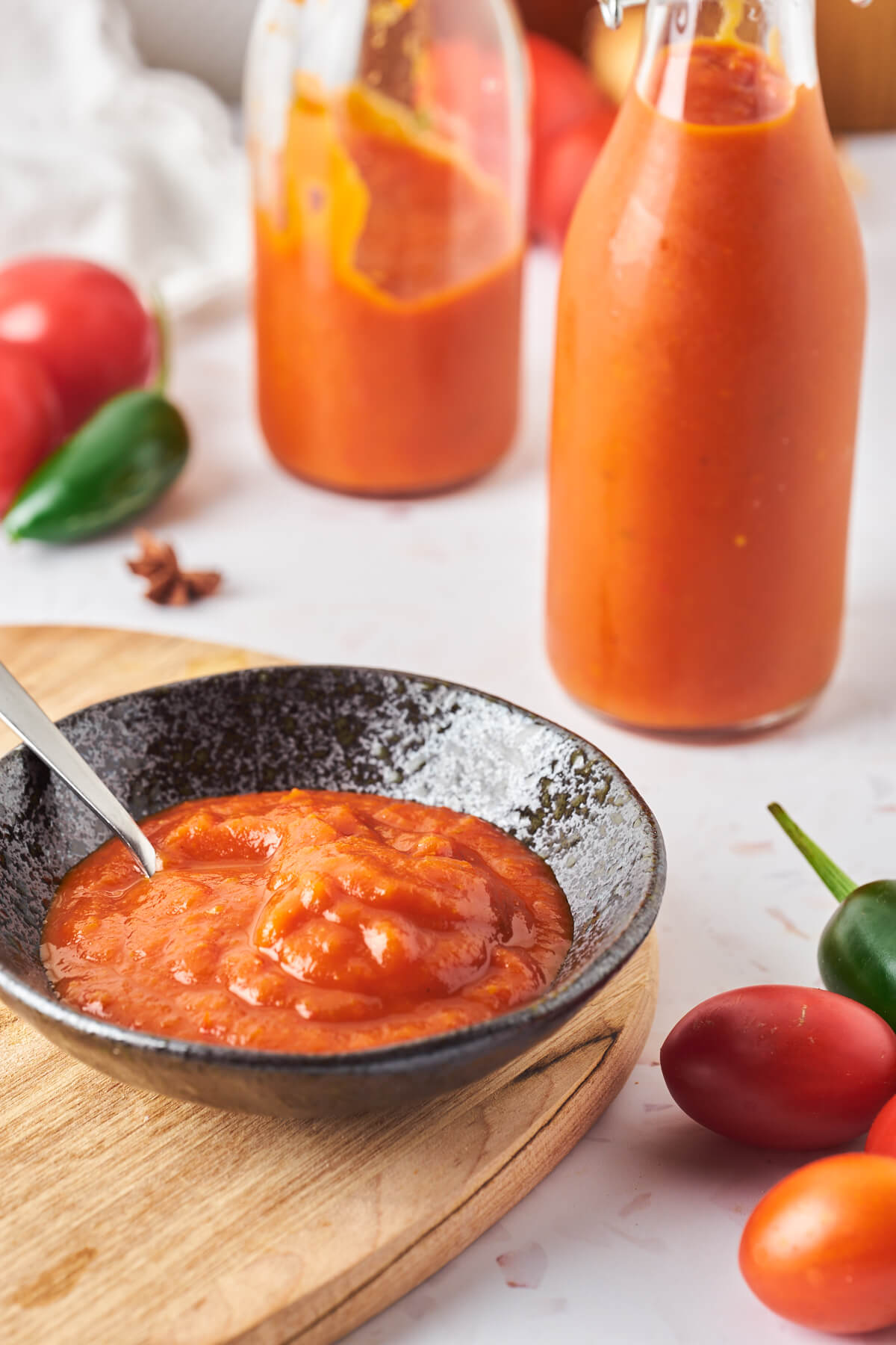 hjemmelavet ketchup i to flasker og lille skål med ketchup samt friske tomater og chili