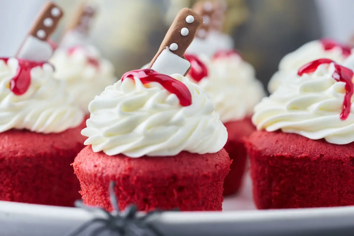 uhyggelige halloween cupcakes med røde muffins, hvid frosting, kniv og blod på toppen