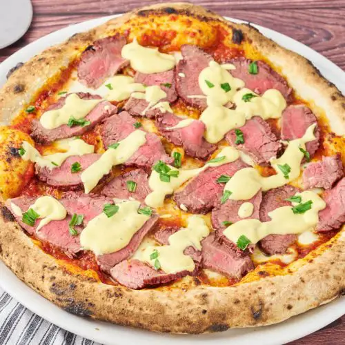 bøf bearnaise pizza på pizzatallerken med pizzaskærer ved siden af