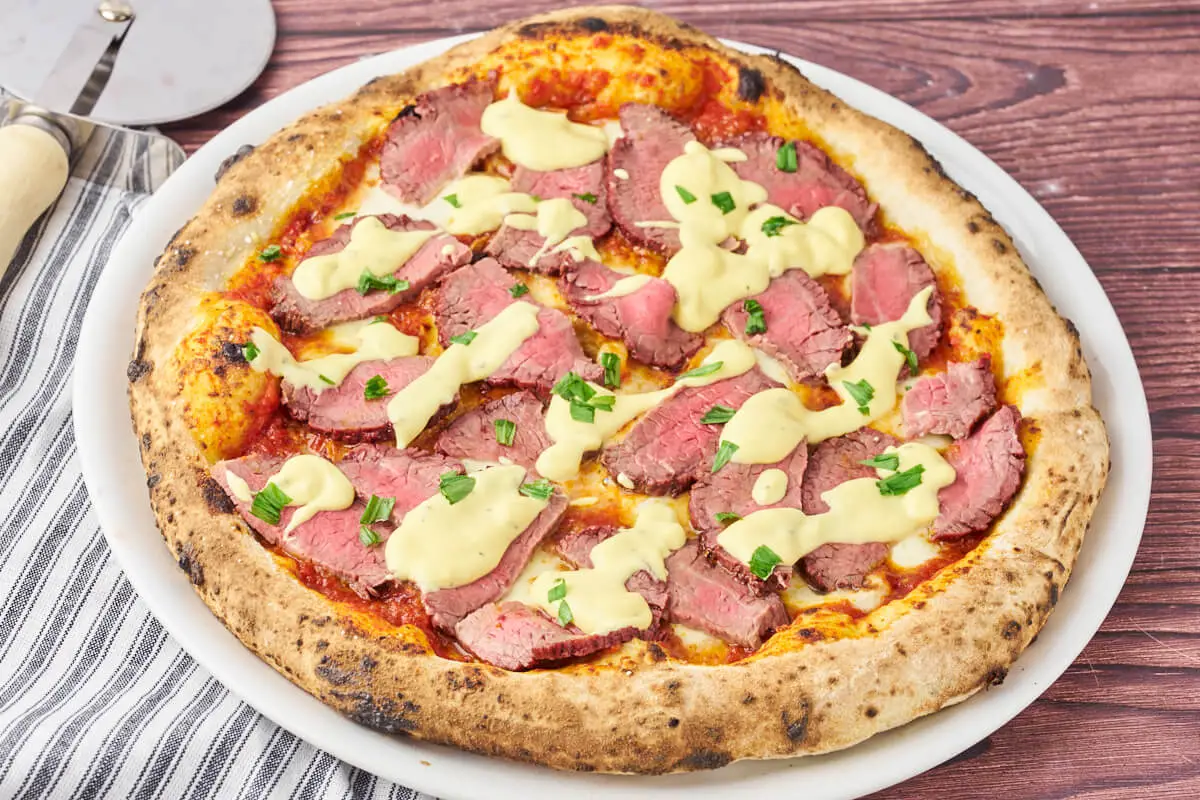 bøf bearnaise pizza på pizzatallerken med pizzaskærer ved siden af
