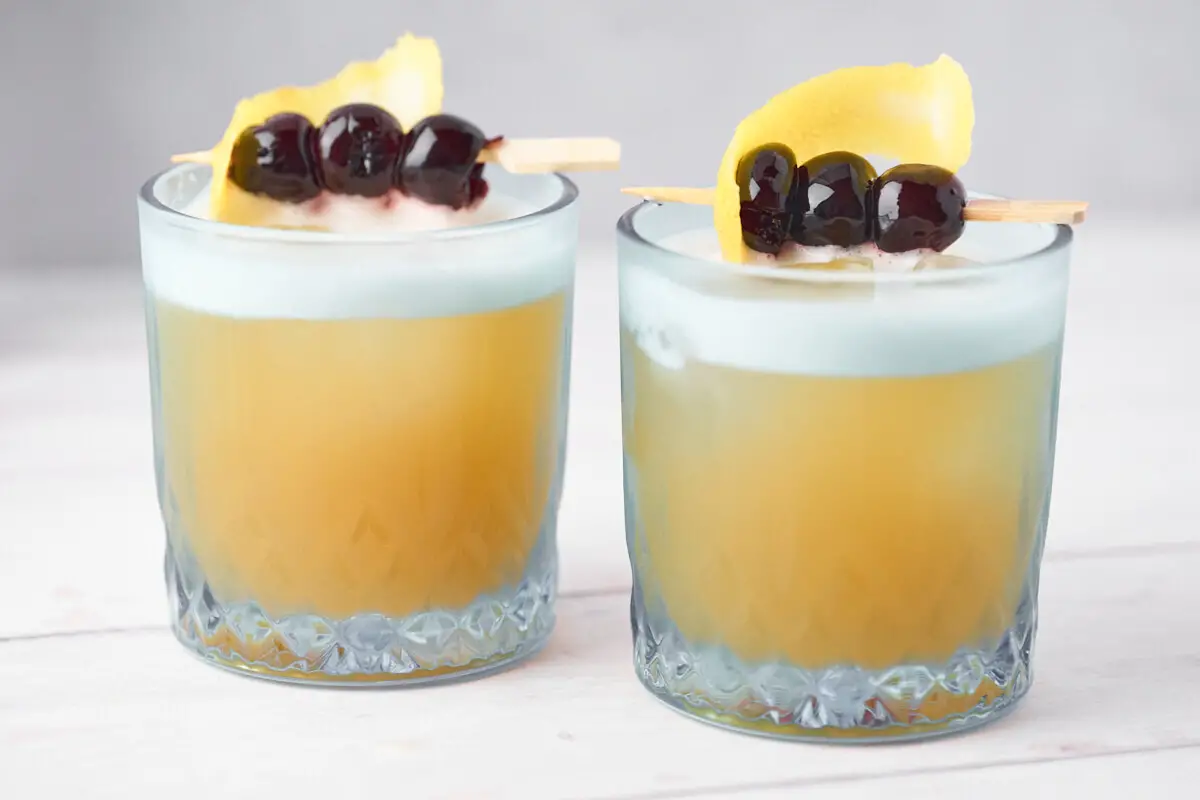 amaretto sour i to glas med citron og kirsebær som garnish