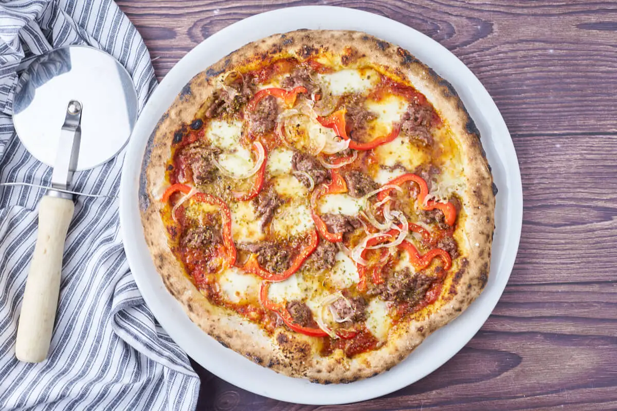 pizza med oksekød og peberfrugt på pizzatallerken med pizzaskærer