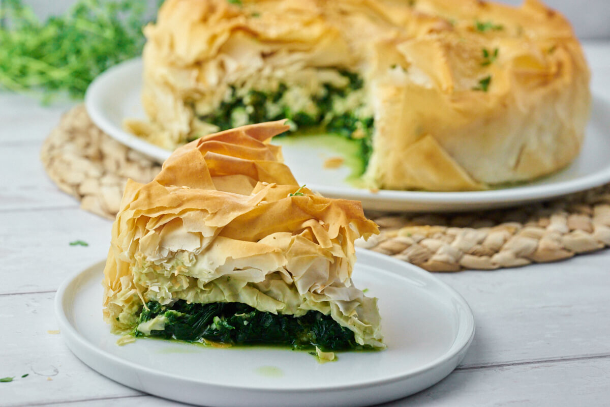 græsk spanakopita med spinat og feta på tallerken med skive af tærten i forgrunden