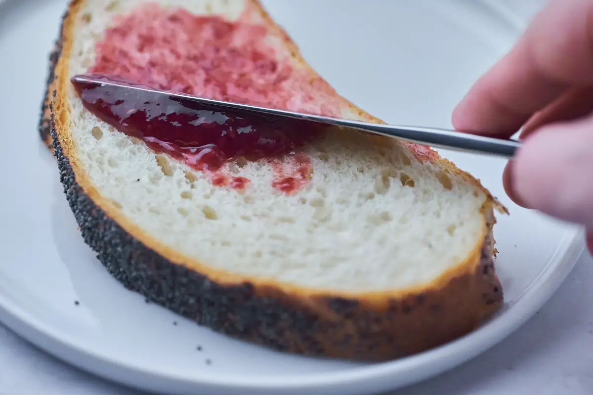 skive franskbrød med marmelade og kniv der smørrer