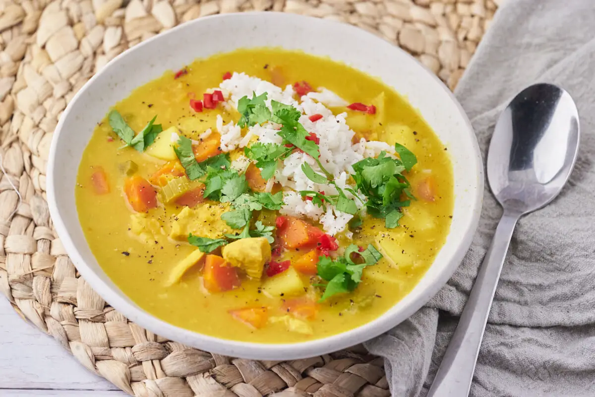 Indisk mulligatawny suppe med kylling og grøntsager i skål med ske ved siden af
