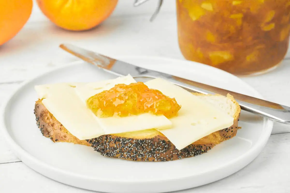 hjemmebagt franskbrød med ost og appelsinmarmelade på tallerken.