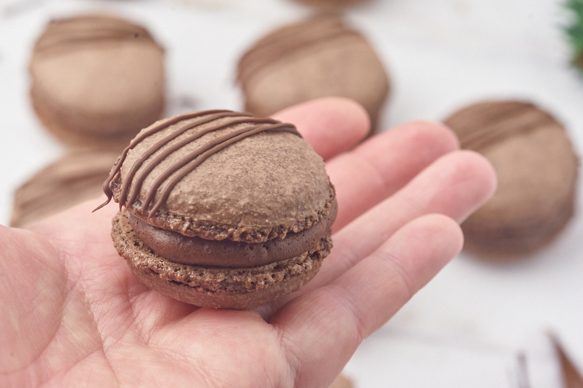 hånd der holder færdig julemacaron med ganache inden i og pyntet med chokolade.