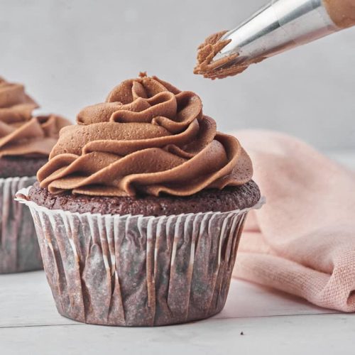 chokoladefrosting der bliver sprøjtet på muffins med en sprøjtepose med stjernetyl.