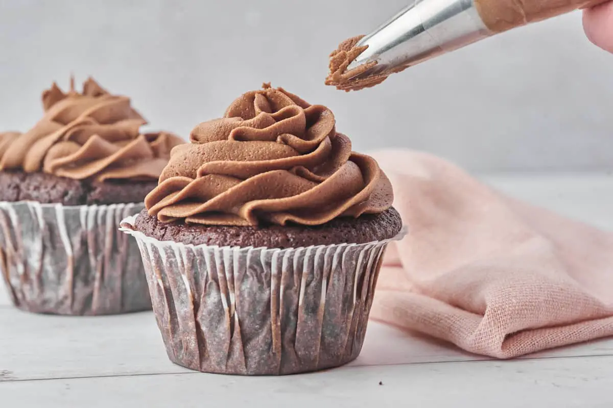 chokoladefrosting der bliver sprøjtet på muffins med en sprøjtepose med stjernetyl.