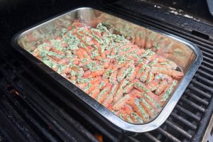 fad med rå jomfruhummerhaler fyldt med smør i en bakke på grillen.