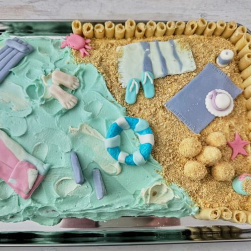 Strandkage med vand, sand og strandudstyr i fondant.