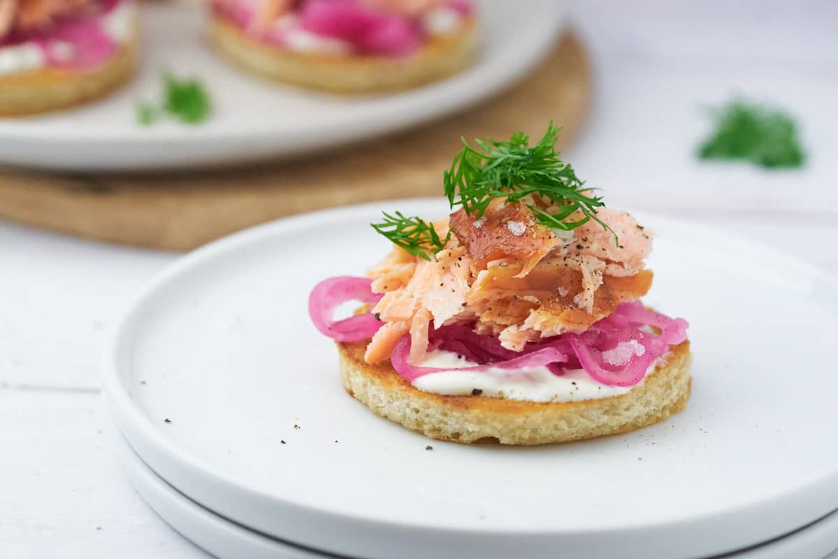 lille forret med rundt stykke ristet brød, creme fraiche, syltede rødløg og varmrøget laks.