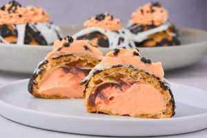 overskåret vandbakkelse så man kan se den hule vandbakkelse, syltetøj og den orange creme.