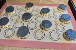 vandbakkelsesdej sprøjtet ud på plade med en skive frossen sort kiksedej på toppen.